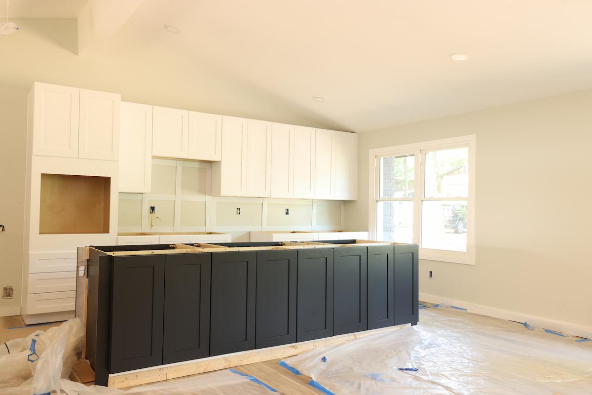 Unfinished kitchen interior with newly installed white wall cabinets, a black base island, and plastic floor protection.
