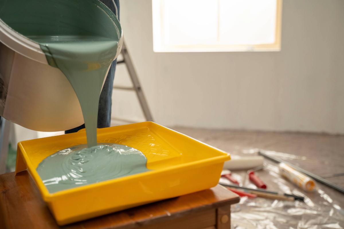 Painter pouring vibrant green paint from a bucket into a bright yellow tray
